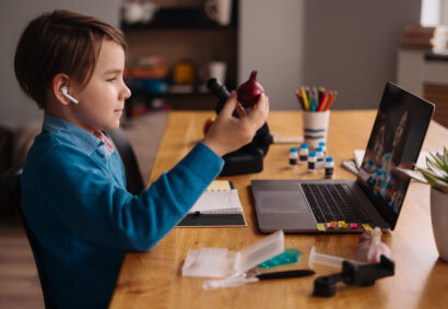 A Preteen boy uses a laptop to make a video call with his teacher. The Screen shows an online lecture with a teacher explaining the subject from class.
